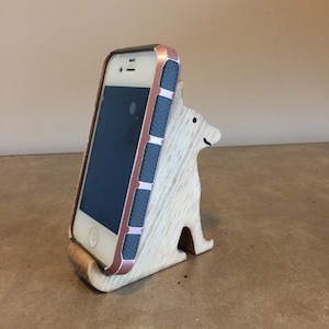 May include: A wooden phone stand shaped like a dog, with a phone in a rose gold case resting in the stand.