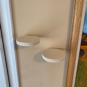 May include: Two round wooden shelves mounted on a light beige wall. The shelves are made of unfinished light wood and are about 6 inches in diameter.