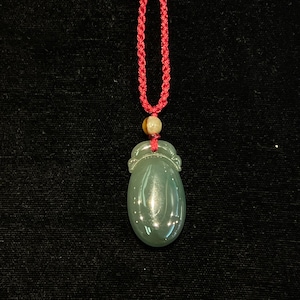May include: A jade pendant in the shape of an egg, with a carved design, hanging from a red cord.