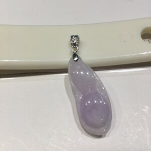 May include: A lavender jade pendant with a silver bail. The pendant is shaped like a long, thin bean.