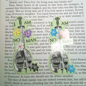 May include: Two handmade green bookmarks with a sword and helmet design, adorned with colorful flowers. The text "I AM NO MAN" is visible on the bookmarks, set against a backdrop of open book pages.