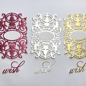 May include: Three sets of die-cut paper embellishments in magenta, silver, and gold. Each set includes an ornate, rectangular filigree frame with a central oval cutout and a separate script word cutout that reads "wish" in matching colors.