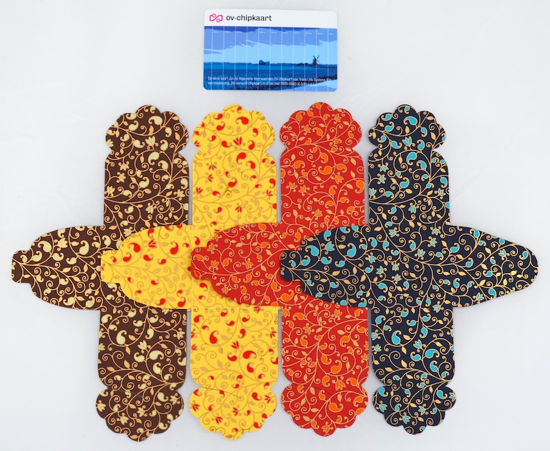 May include: Four favor boxes with a paisley pattern in brown, yellow, orange, and blue. The boxes are made of paper and have a scalloped edge.