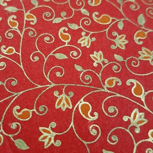 May include: Red fabric with a gold paisley pattern. The pattern features intricate swirls and leaves.