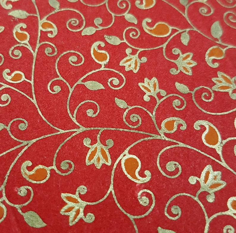 May include: Red fabric with a gold paisley pattern. The pattern features intricate swirls and leaves.