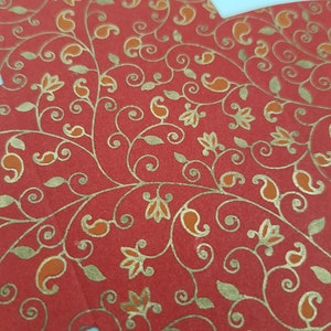 May include: Red paper with a gold floral pattern. The pattern features paisley shapes, leaves, and flowers.