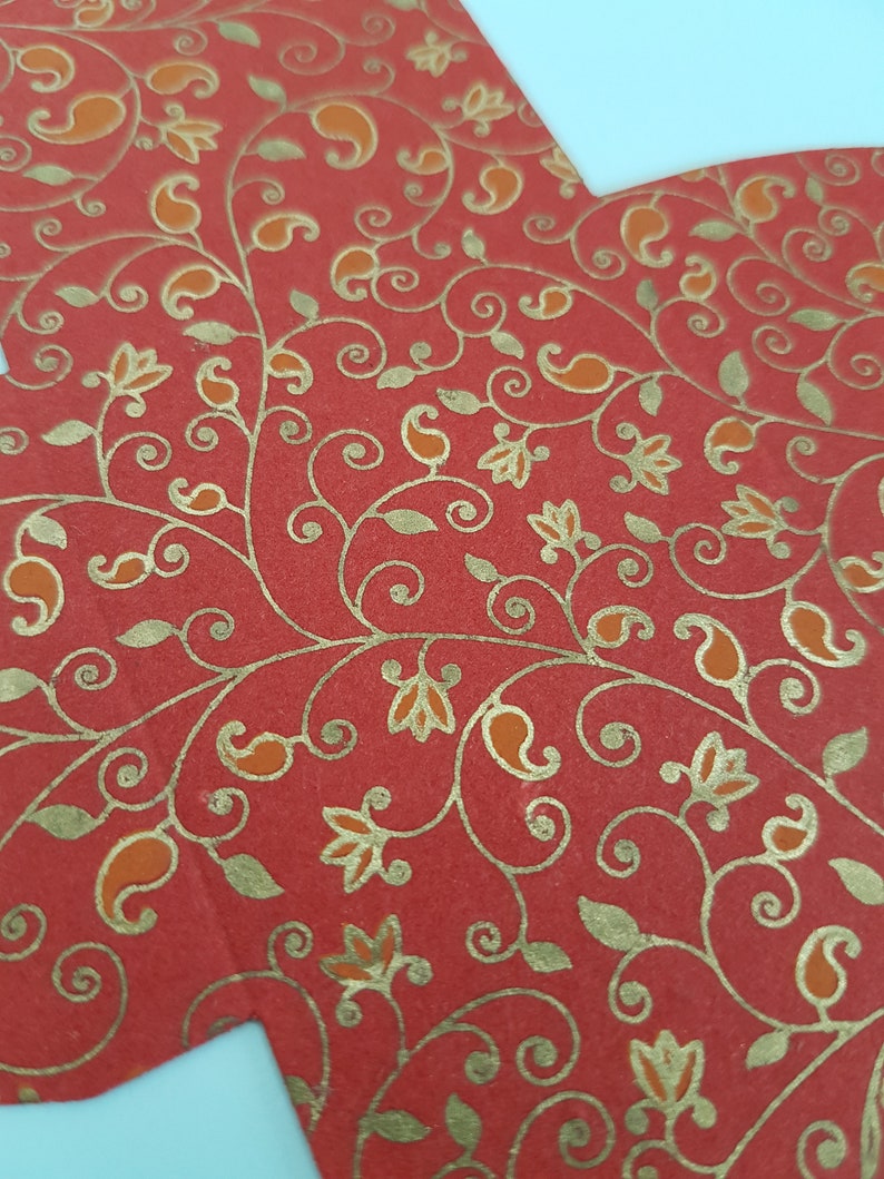 May include: Red paper with a gold floral pattern. The pattern features paisley shapes, leaves, and flowers.