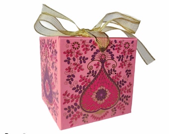 Puede incluir: Una caja de regalo rosa con una cinta dorada y un diseño floral. La caja tiene un diseño en forma de corazón en el centro con detalles dorados.
