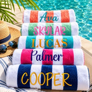 May include: A stack of five rolled beach towels with white and colored stripes. Each towel features a personalized name embroidered in a contrasting thread color: Ava in teal, Skylar in pink, Lucas in gold, Palmer in purple, and Cooper in gold.