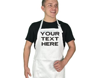 May include: White apron with the text "YOUR TEXT HERE" in black. The apron has two front pockets and a white neck strap. The person in the image is wearing a black t-shirt.