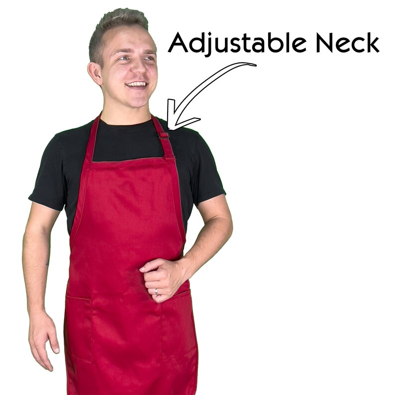 Może przedstawiać: Gładki czerwony fartuch z regulowanym paskiem na szyję. Fartuch ma dwie przednie kieszenie i jest noszony na czarnym t-shircie. Tekst "Adjustable Neck" znajduje się nad paskiem fartucha.