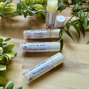May include: Four different flavored lip balms in tubes with floral designs and text that reads "Tallow Lip Balm" and the flavor of each balm: "Huckleberry", "Peach Vanilla", "Peppermint", and "Strawberry".