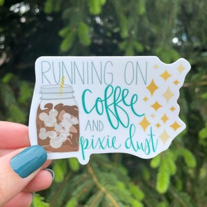 May include: White sticker with a teal green mason jar filled with coffee and a straw. The text "Running on Coffee and Pixie Dust" is written in teal green with gold glitter accents.