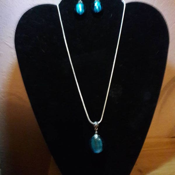 parure constituée d'un collier argenté avec pendentif galet en verre bleu et les boucles d'oreilles assorties, dans un style vintage.