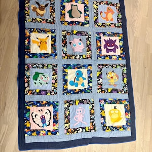 May include: A blue and white patchwork quilt with various Pokemon characters embroidered on each square. The quilt is edged with a dark blue border.