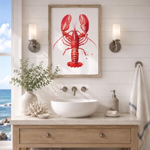 May include: A framed wall art print featuring a vibrant red watercolor illustration of a lobster centered on a white background. The artwork is displayed above a white vessel sink, a light-colored wooden vanity, and two wall-mounted light fixtures.