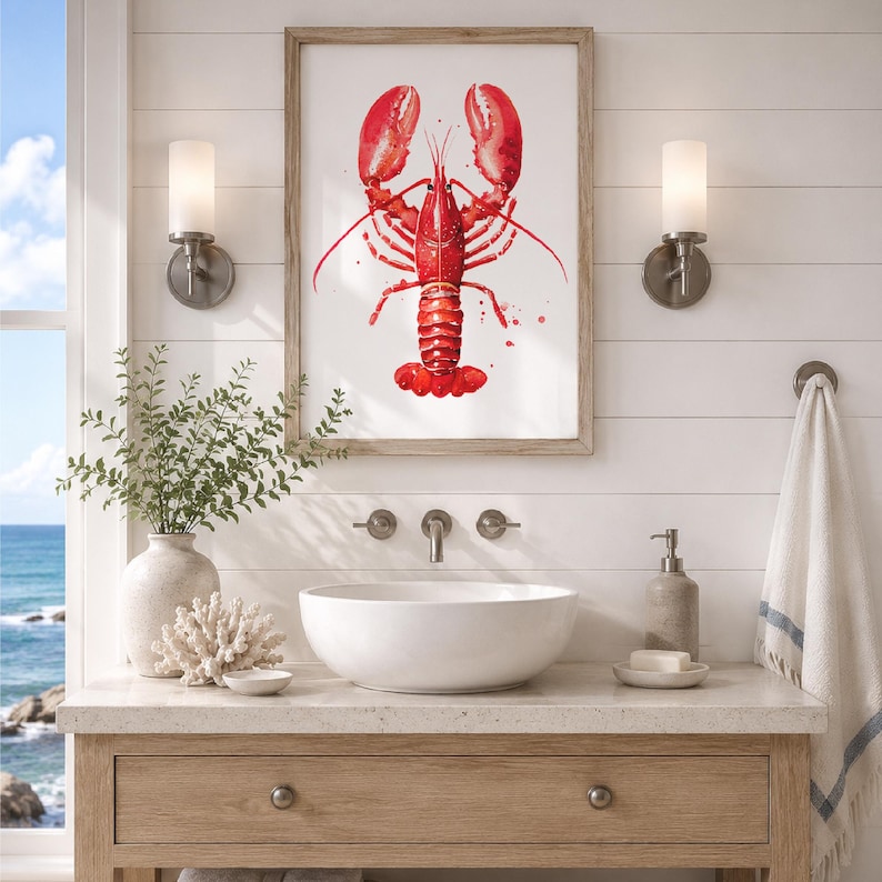 May include: A framed wall art print featuring a vibrant red watercolor illustration of a lobster centered on a white background. The artwork is displayed above a white vessel sink, a light-colored wooden vanity, and two wall-mounted light fixtures.