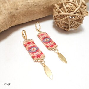 May include: A pair of gold hoop earrings with a beaded rectangular pendant featuring a geometric pattern in shades of pink, red, and purple. The pendant is attached to a gold leaf-shaped charm.
