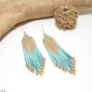 Peut inclure: Longues boucles d'oreilles pendantes en perles avec un dégradé de perles turquoise et dorées. Les boucles d'oreilles ont un motif géométrique en haut et des crochets dorés.