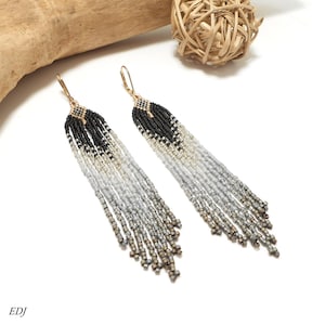 May include: A pair of long fringe earrings featuring a gradient pattern of small glass beads. The design transitions from solid black at the top to metallic silver, light gray, and dark gray at the bottom, finished with gold-tone lever back hooks.
