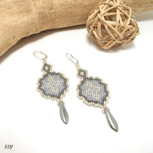 May include: A pair of silver dangle earrings with a geometric design made of gray and white beads. The earrings have a teardrop-shaped bead at the bottom.