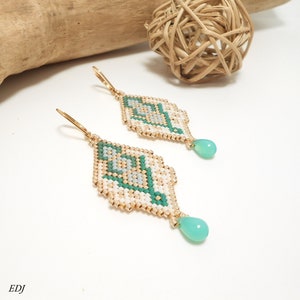 May include: A pair of gold beaded earrings with a geometric design in white, green, and gold. Each earring has a teardrop-shaped light green stone hanging from the bottom.