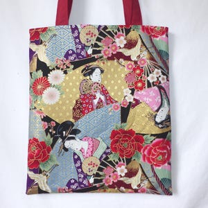 Könnte beinhalten: Tragetasche mit japanisch inspiriertem Design. Der Stoff zeigt einen farbenfrohen Druck von Geishas, Fächern und floralen Mustern in Rot, Gold, Rosa und Blau. Die Tasche hat rote Griffe.