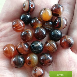 Puede incluir: Una colección de 20 cuentas de ágata en tonos marrones, rojos y negros con rayas blancas. Las cuentas tienen 8 mm de diámetro y un agujero perforado en el centro.