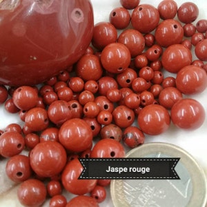 Peut inclure: Gros plan sur une collection de perles de jaspe rouge. Les perles sont lisses et polies, et ont un aspect naturel et terreux. Le texte "Jaspe rouge" est visible sur l'image.