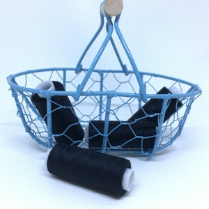 Könnte beinhalten: Ein blauer Drahtkorb mit einem Holzgriff, gefüllt mit schwarzen Garnrollen.