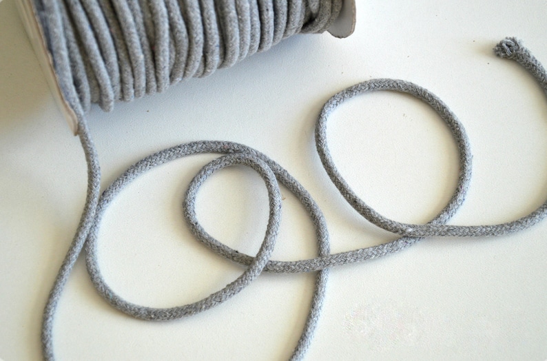 May include: A spool of gray cotton cord with a few loops of cord lying on a white surface.