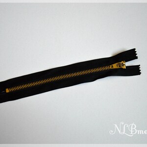 May include: A black zip with a gold-coloured metal pull and teeth. The zip is open, showing the teeth. This is a sewing notion, used for clothing and other fabric projects.