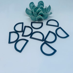 May include: A group of ten dark blue metal D-rings, scattered on a white surface. The rings are all the same size and shape.