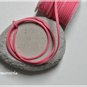 Może przedstawiać: Różowy sznurek ze skóry zamszowej owinięty wokół szarego kamienia. Sznurek ma około 3 mm szerokości.