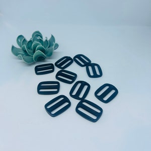 Peut inclure: Dix boucles coulissantes en plastique noir. Les boucles sont rectangulaires avec deux lignes parallèles au centre.