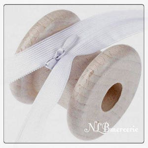 May include: A spool of white elastic with a zipper pull. The elastic is wound around a wooden spool.