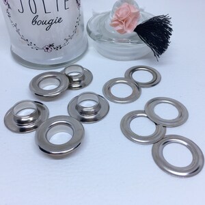 Op de afbeelding: Tien zilveren metalen oogjes voor knutsel- en doe-het-zelfprojecten. De oogjes hebben een ronde vorm met een gat in het midden.