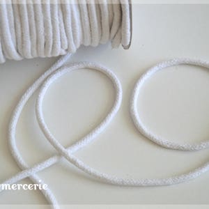 May include: White cotton cord, a spool of the cord is in the background, and the cord is looped in the foreground.  The text "NLBmercerie" is in the lower left corner of the image.