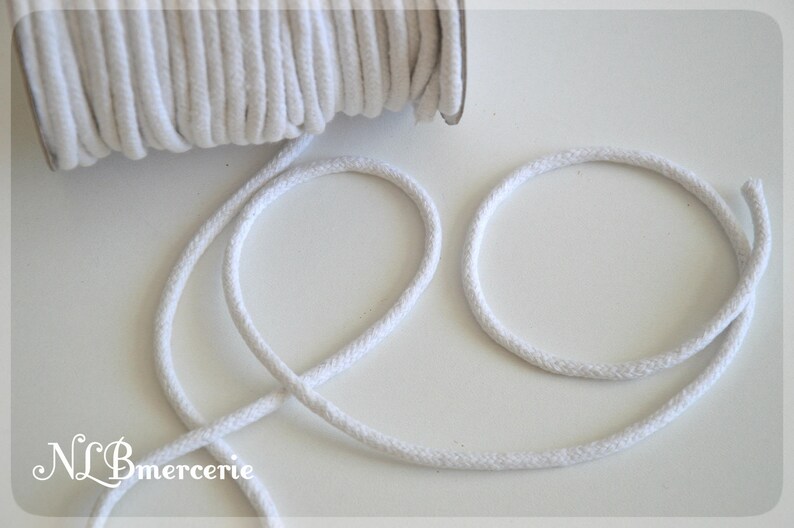 May include: White cotton cord, a spool of the cord is in the background, and the cord is looped in the foreground.  The text "NLBmercerie" is in the lower left corner of the image.