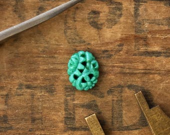 May include: A teal green carved button with a floral design. The button is on a wooden surface with a metal measuring tool.