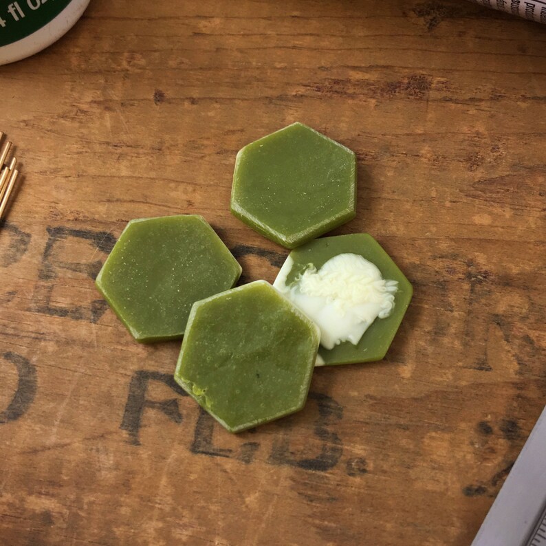 May include: Four hexagonal green and white soap bars on a wooden surface.