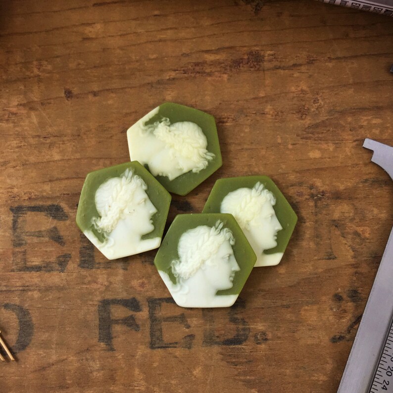 May include: Four green and white cameo-style hexagonal buttons with a profile of a person wearing a crown.
