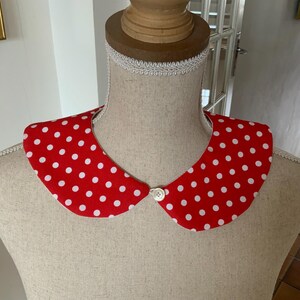 Peut inclure: Un col en tissu à pois rouge et blanc avec une fermeture à bouton blanc.