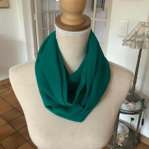 Op de afbeelding: Een teal groene oneindigheidssjaal gemaakt van een zachte, vloeiende stof. De sjaal is om de nek van een mannequin gelegd.
