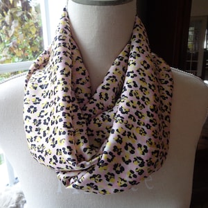 Könnte beinhalten: Ein rosafarbener, gelber und schwarzer Leopardenmuster-Infinity-Schal. Der Schal ist aus einem weichen, seidenartigen Material gefertigt.