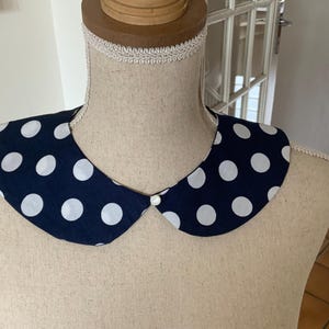 Peut inclure: Un col en tissu bleu marine à pois blancs avec un bouton blanc au centre.