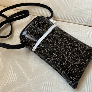 Peut inclure: Un sac à bandoulière noir pour téléphone avec une bande blanche et des paillettes dorées. Le sac a une fermeture éclair et une longue sangle réglable.