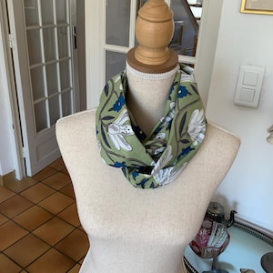 Könnte beinhalten: Ein grün-blau-weiß gemusterter Schal mit floralem Muster und einem gedrehten Design. Der Schal wird auf einer Schaufensterpuppe präsentiert.