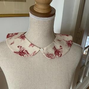 Peut inclure: Un col claudine en coton blanc avec un motif toile rouge et blanc représentant une femme à cheval. Le col a une fermeture boutonnée.