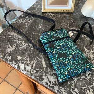 Könnte beinhalten: Eine schwarze Umhängetasche mit Reißverschluss und einem langen, verstellbaren Trageriemen. Die Tasche ist aus Stoff mit einem Muster aus blauen Eulen auf grünem und schwarzem Hintergrund. Die Tasche hat ein kleines Etikett mit der Aufschrift "Hand".